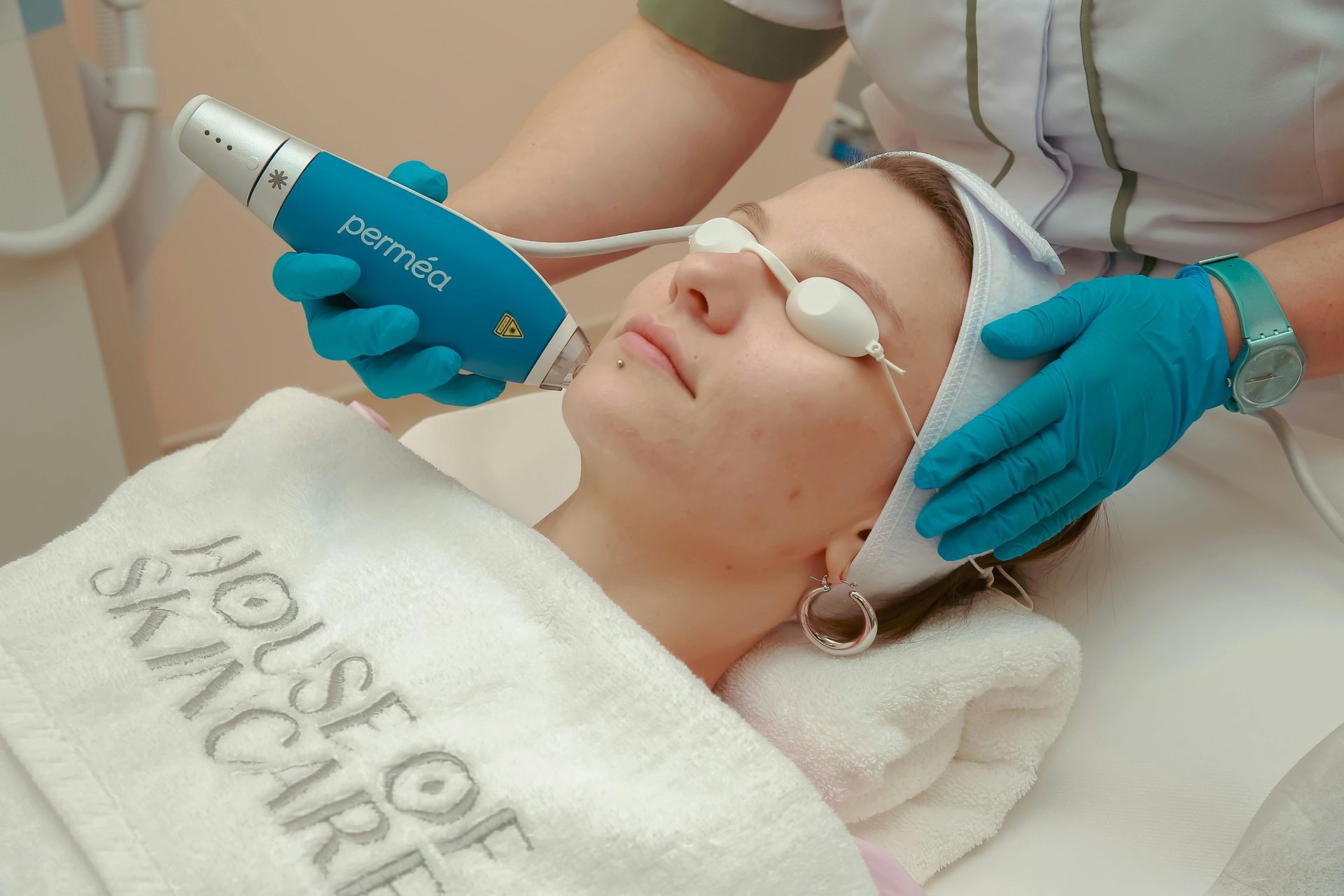 Woman receiving laser skin treatment at a spa, wearing safety glasses and headband, with a gloved technician.
