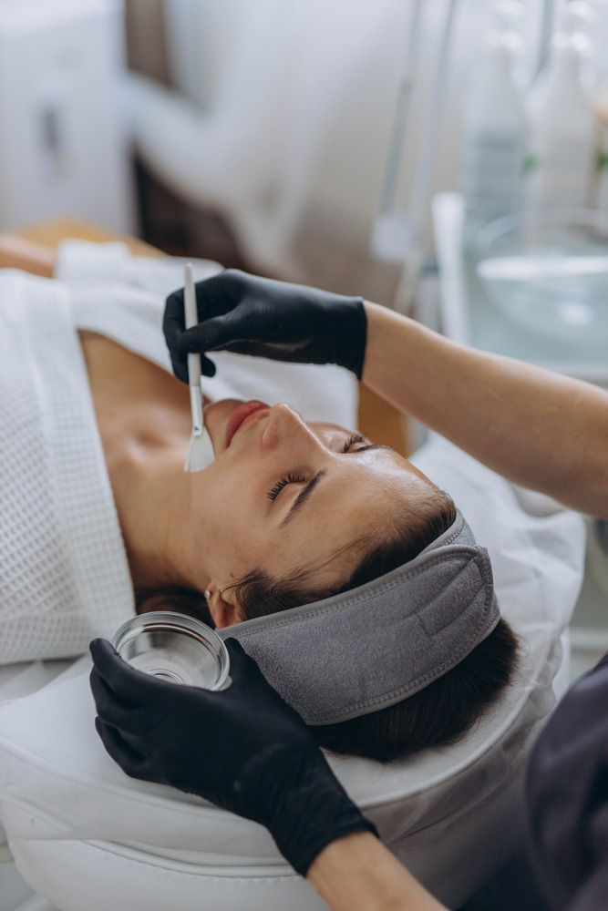 Woman receiving dermaplaning facial; esthetician with gloved hands, black bed.