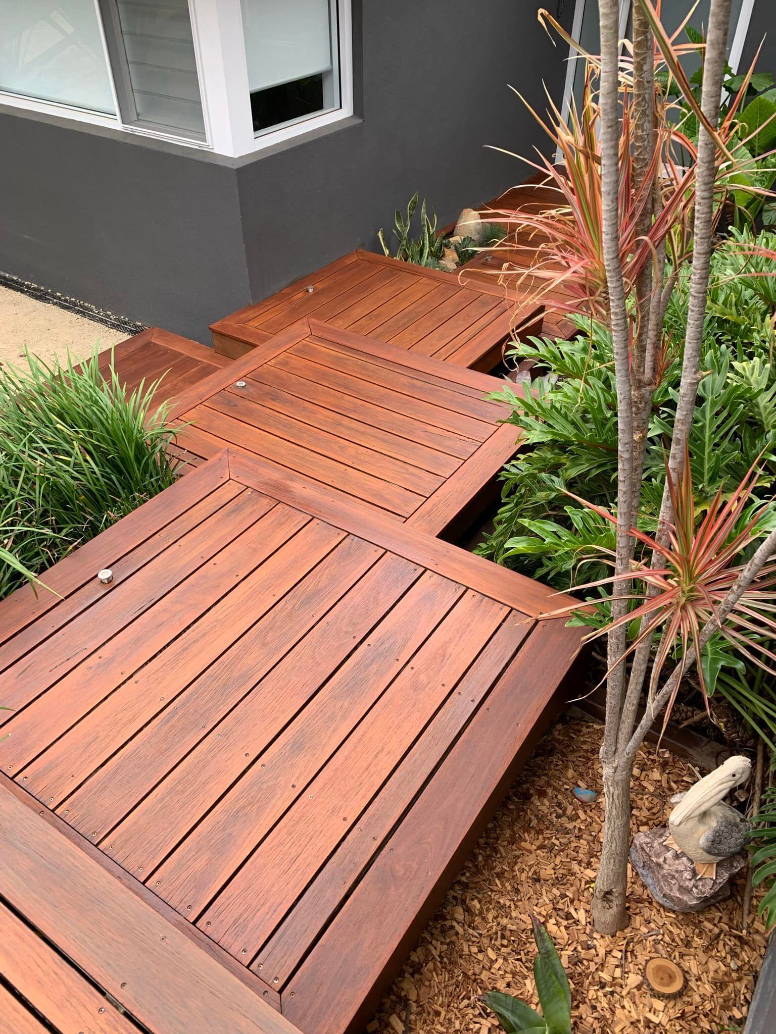 A wooden deck stairway leads up to a modern home, surrounded by lush green plants and garden mulch  — Custom Floor Sanding In Somersby, NSW