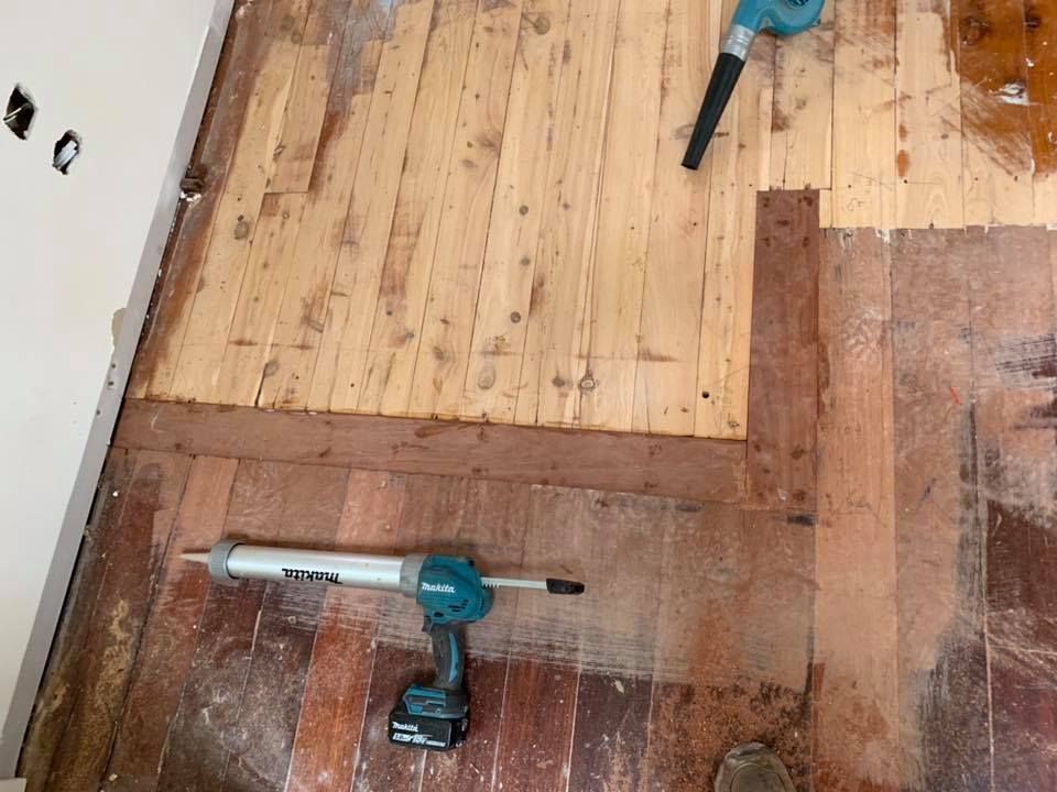 Floor repair in progress; exposed wooden boards, caulking gun, and blower present — Custom Floor Sanding In Somersby, NSW