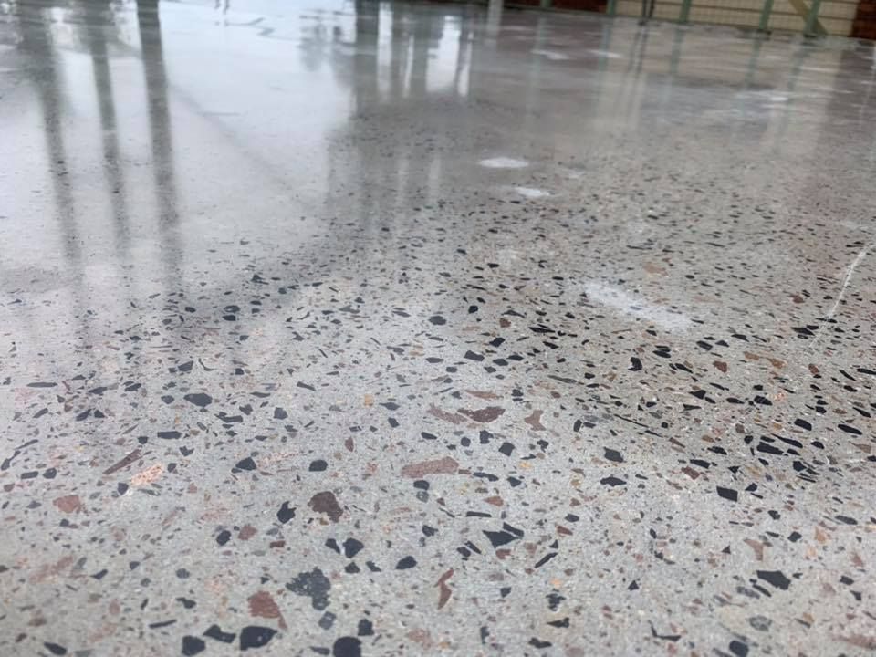 A close-up view of a high-gloss polished concrete floor with exposed grey, black, and brown aggregate stones  — Custom Floor Sanding In Somersby, NSW