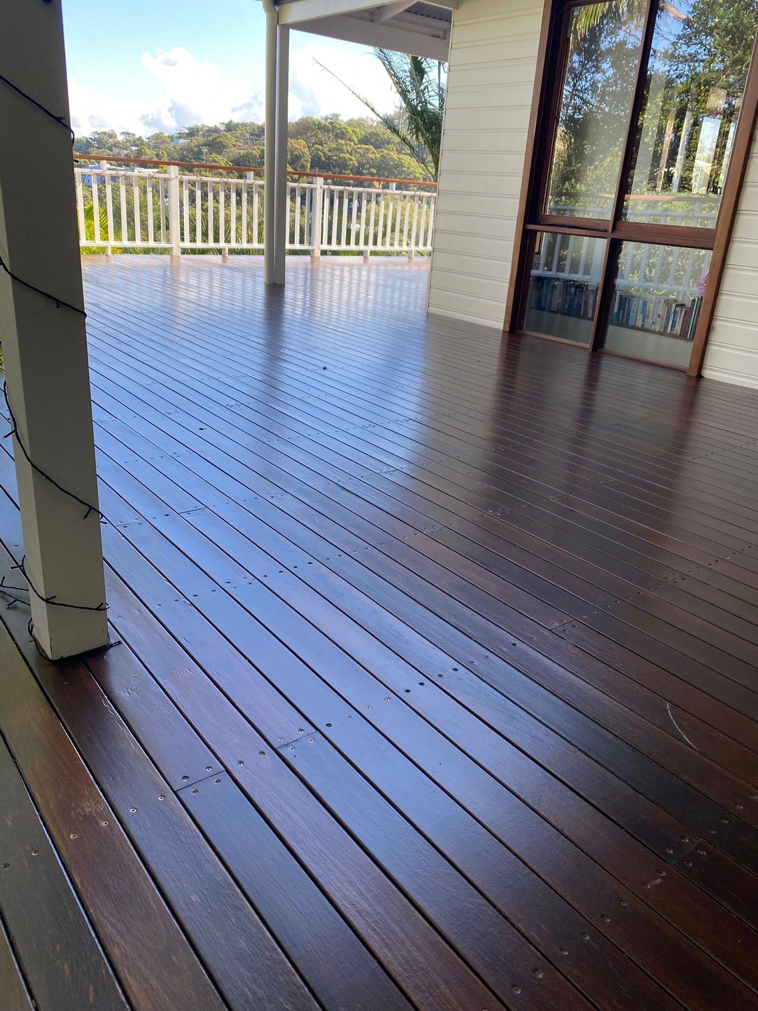 A dark-stained wooden deck with a radiating pattern of screws, viewed from a porch looking toward a white railing  — Custom Floor Sanding In Somersby, NSW