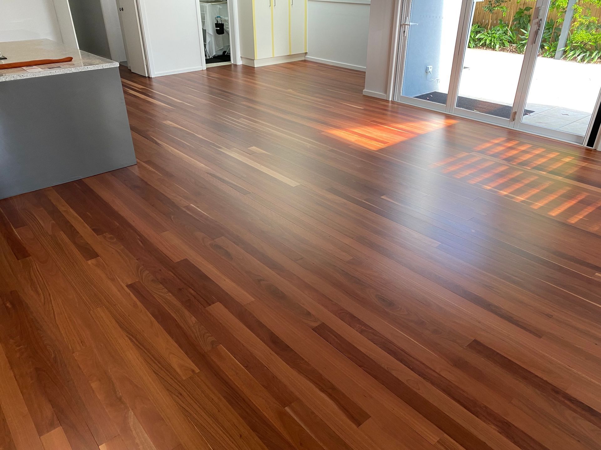 Polished wood flooring in a brightly lit room with a view of an outdoor patio through sliding glass doors — Custom Floor Sanding In Somersby, NSW