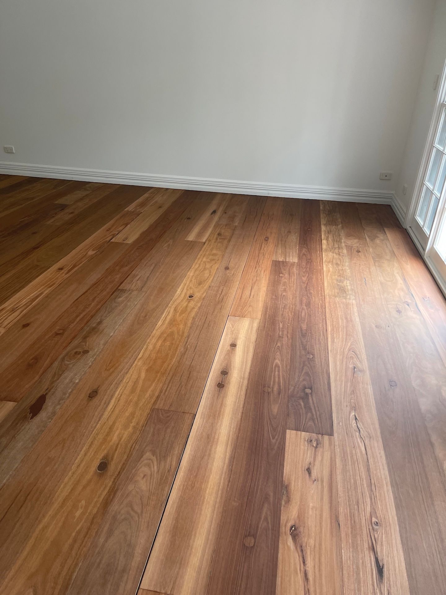 Wooden floorboards in a room with white walls, baseboards, and a window — Custom Floor Sanding In Somersby, NSW