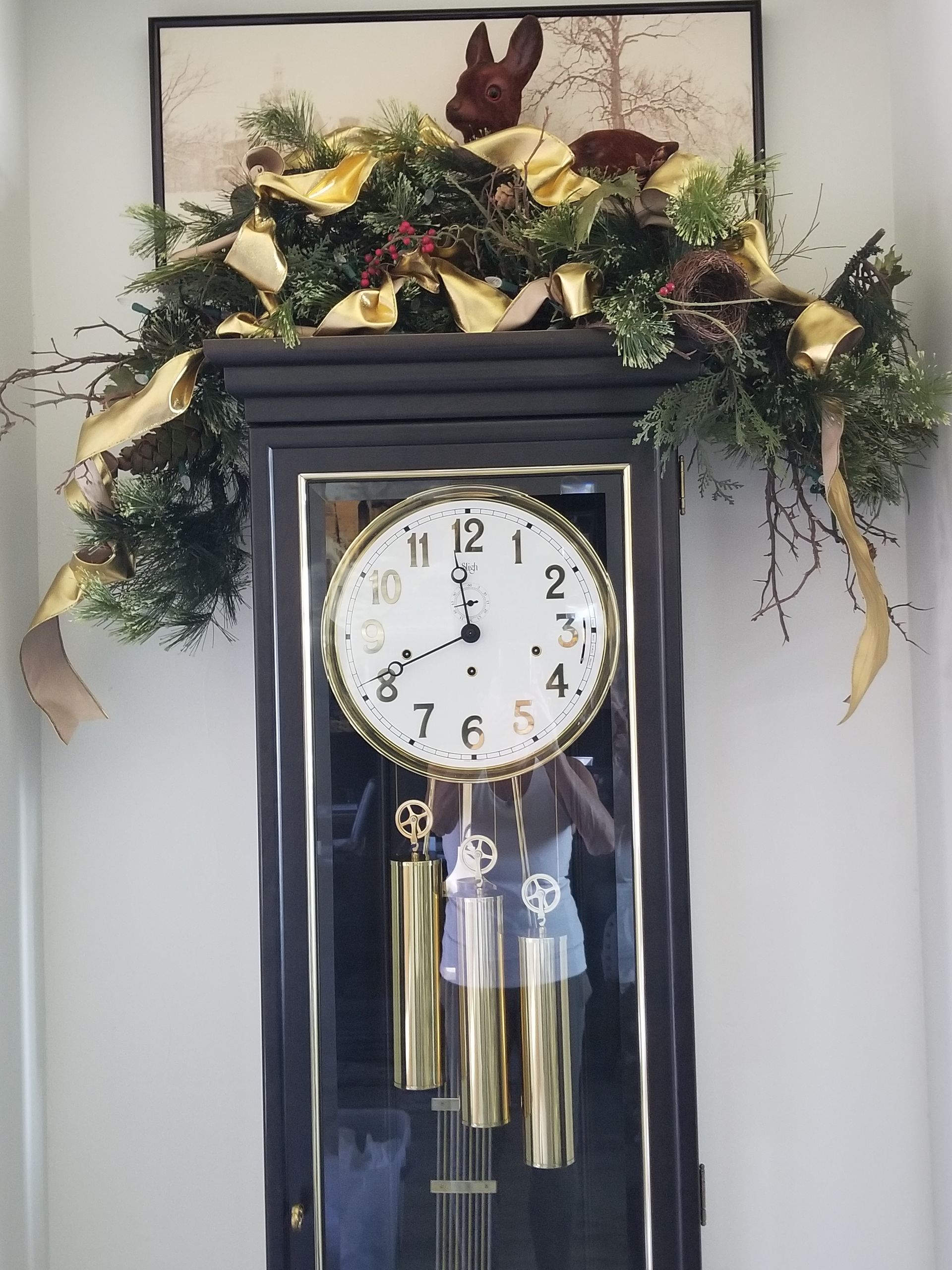 A grandfather clock decorated with gold ribbons and greenery