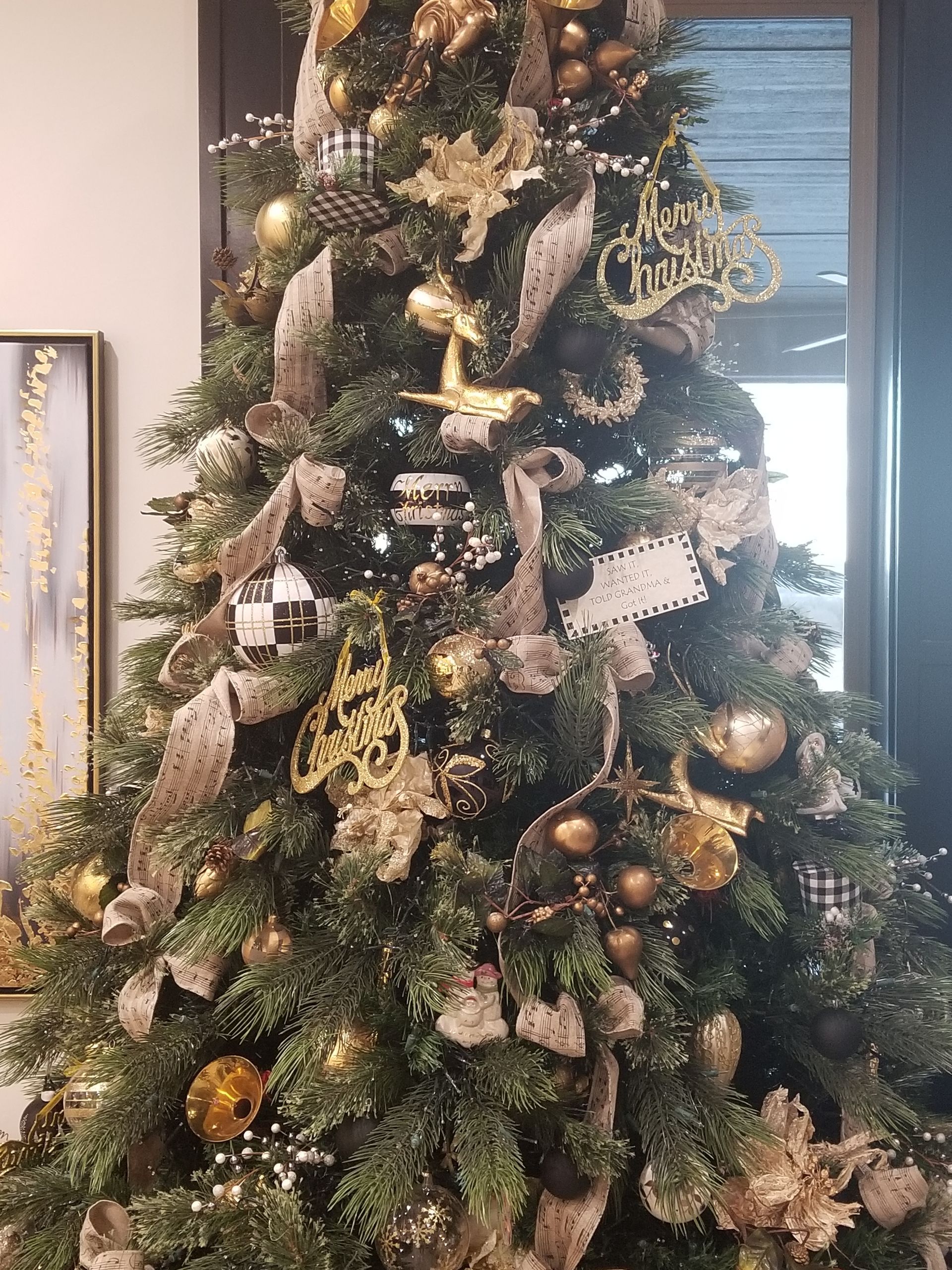 A Christmas tree is decorated with gold decorations and a sign that says Merry Christmas.