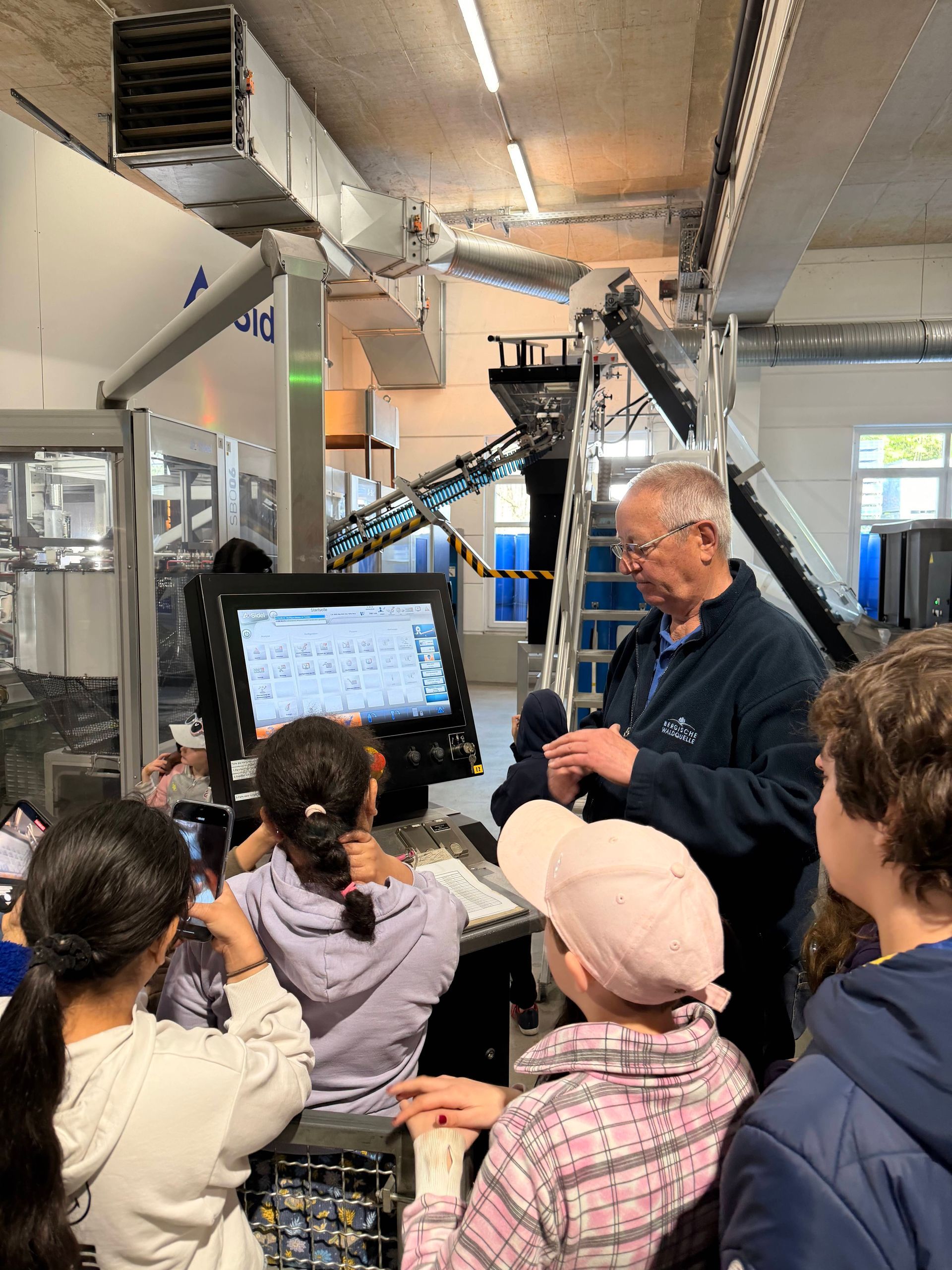 An instructor explains a large industrial machine control panel to a group of students in a workshop.