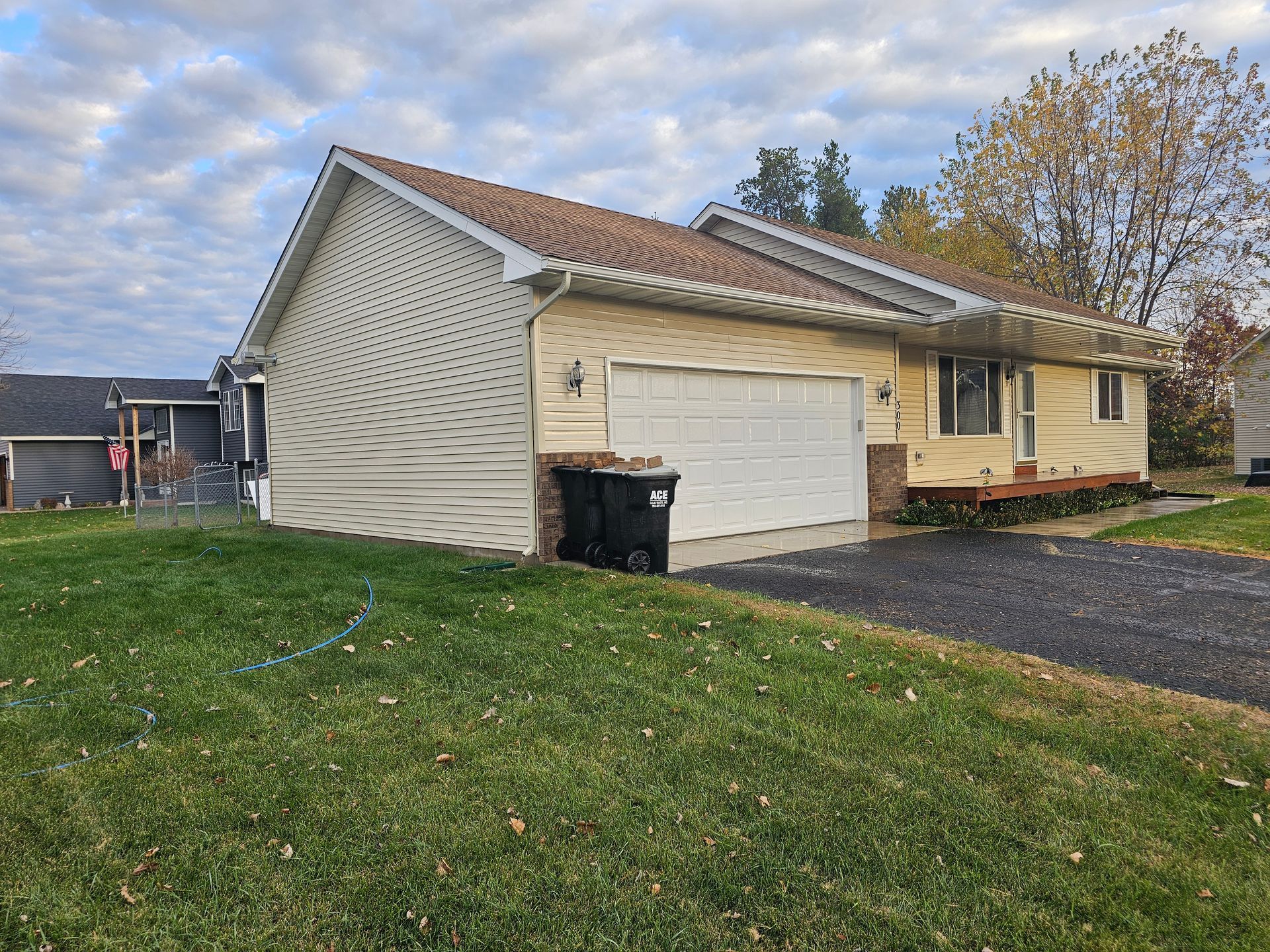 A light yellow single-story suburban house with a two-car garage, a grassy front yard, and a cloudy sky.