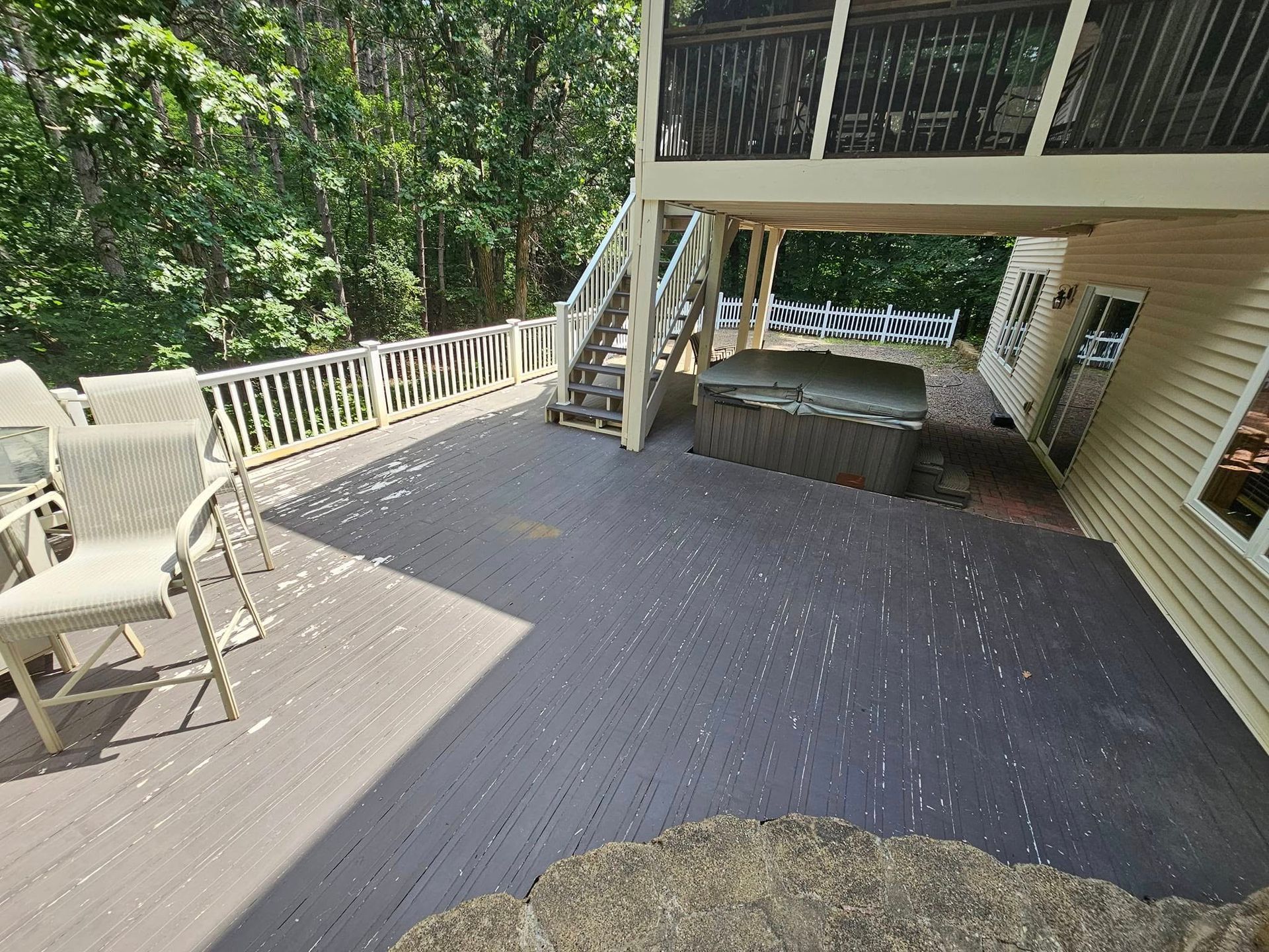 Wooden deck with hot tub, chairs, and stairs to a screened porch, surrounded by trees.