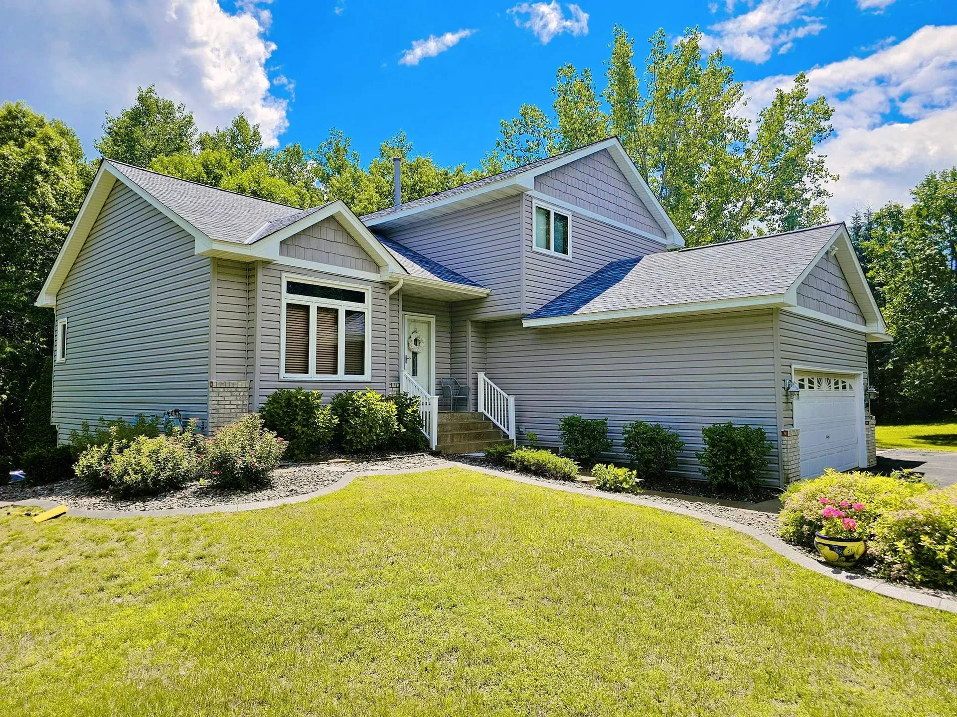 Gray two-story house with a green lawn, blue sky, and trees in the background.