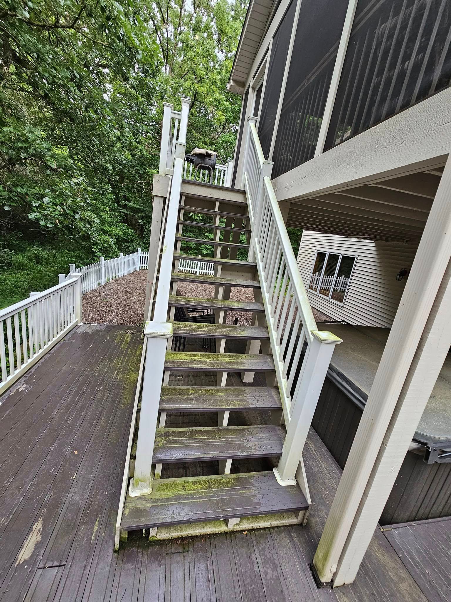 Wooden outdoor stairs leading to a screened porch, surrounded by a deck and trees, with visible weathering and moss.