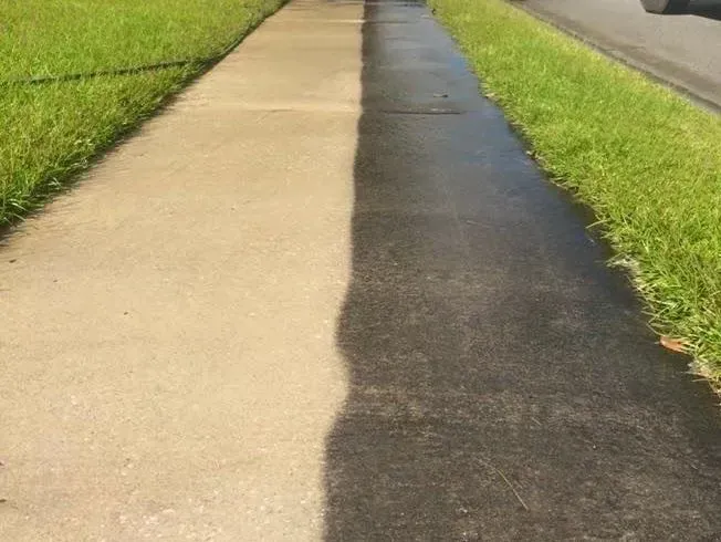 Sidewalk split, one side dirty beige, other side cleaned black, with green grass flanking.