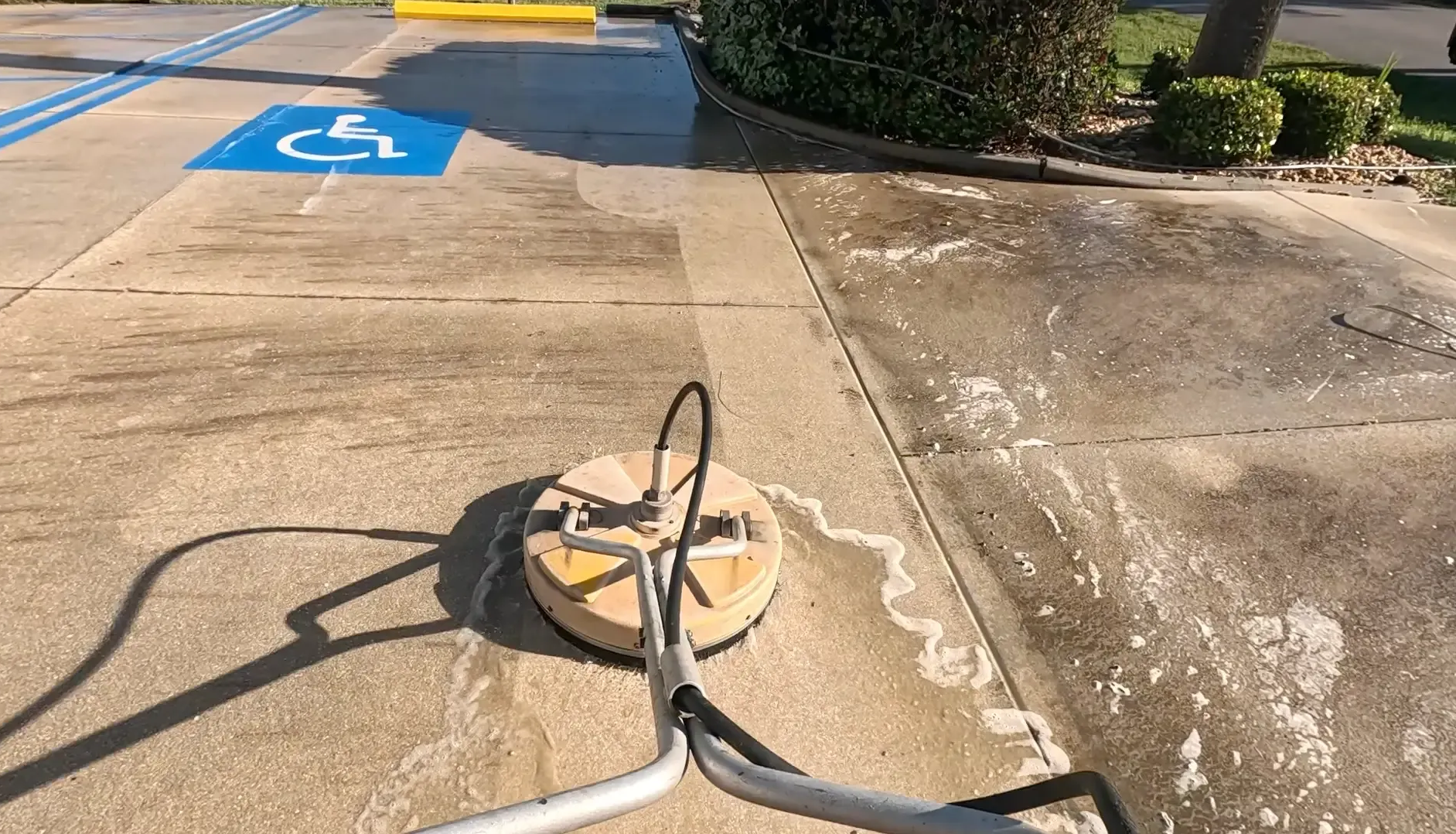Power washer cleaning a concrete surface, revealing a lighter color. Blue handicap symbol visible.