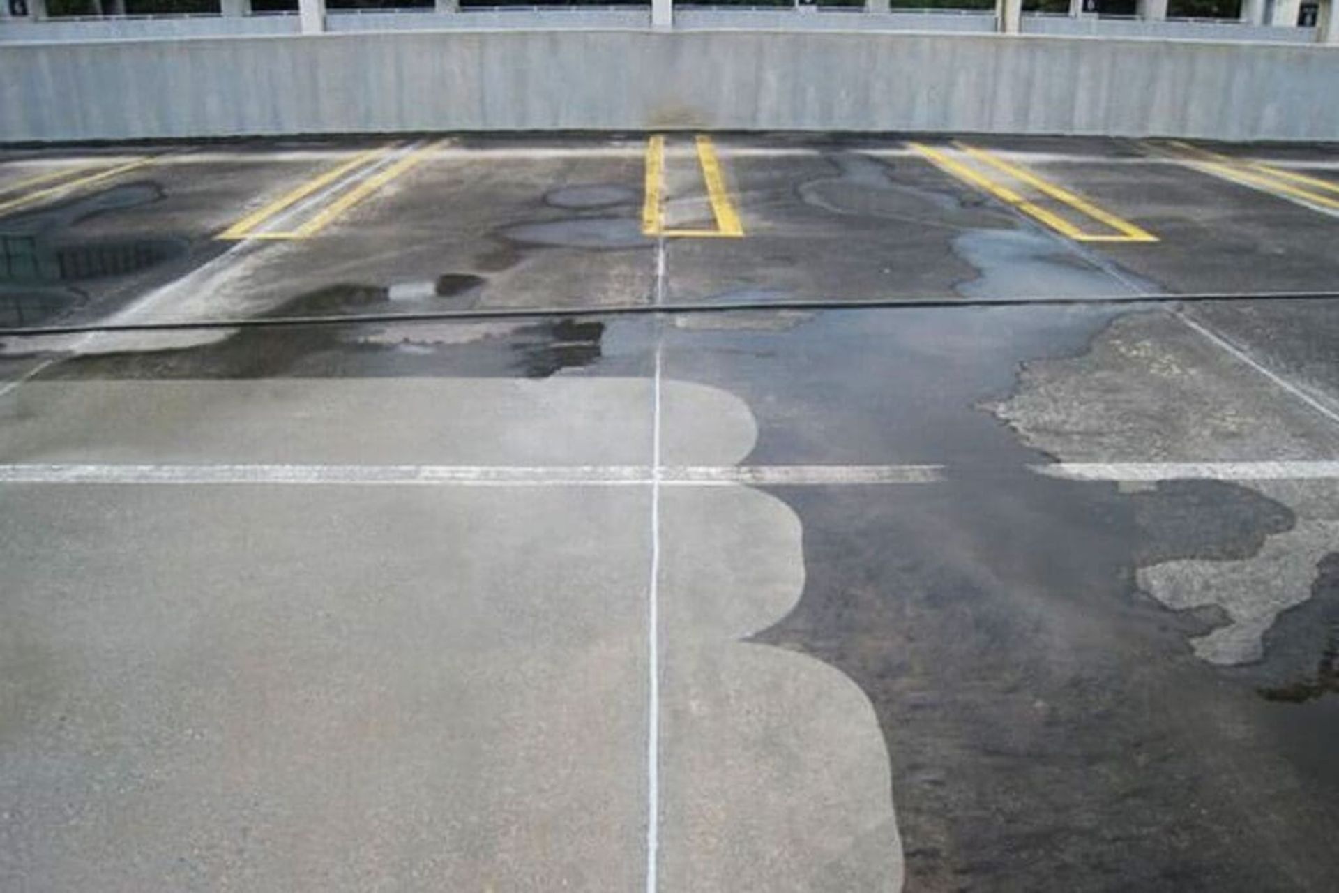 Parking garage floor, partially cleaned with water. Gray concrete, yellow lines, wet and dry areas.