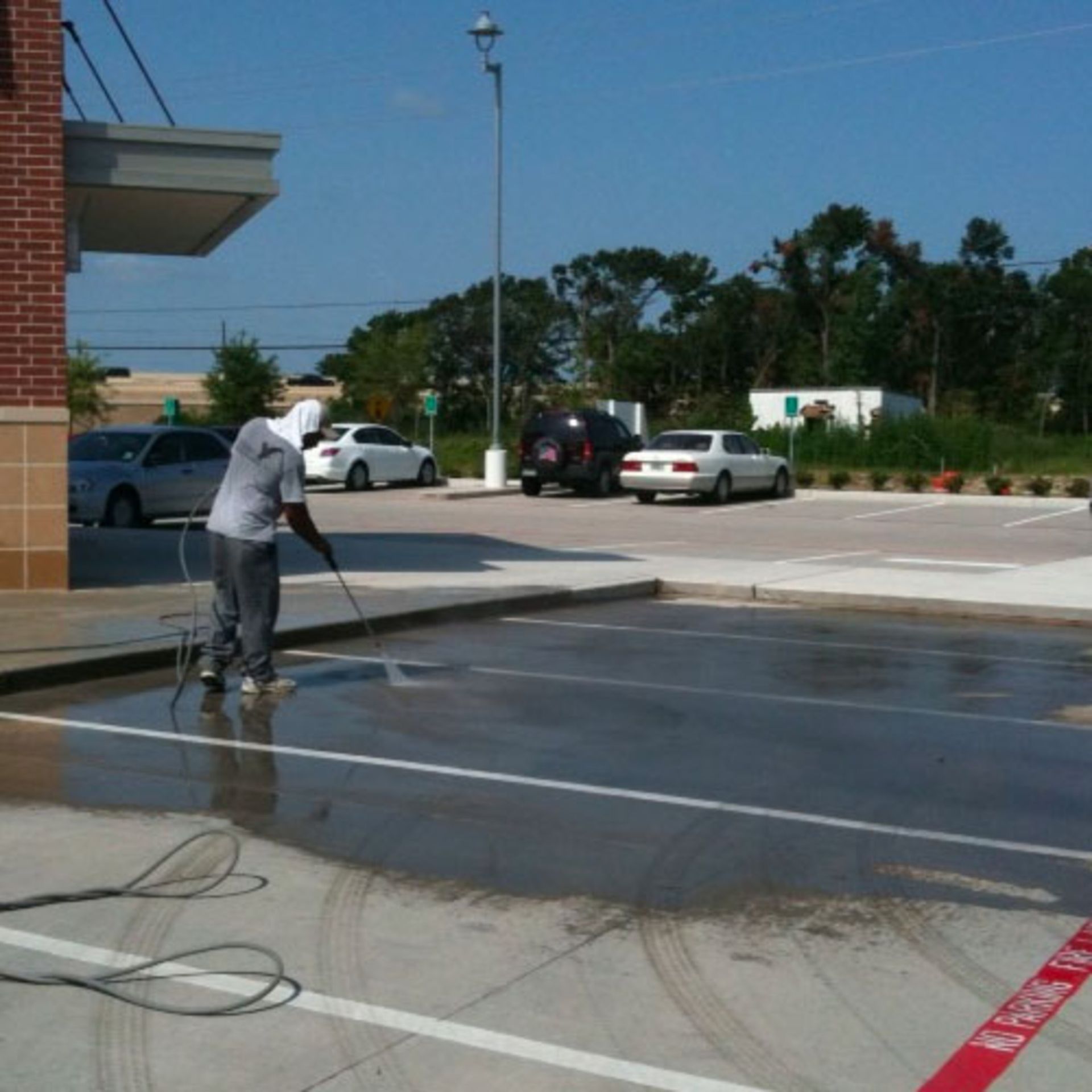 Person power washing a parking lot next to a brick building on a sunny day.