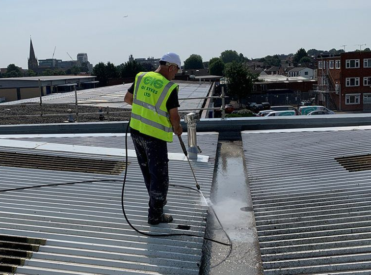 Man in safety vest power washing a corrugated metal roof.