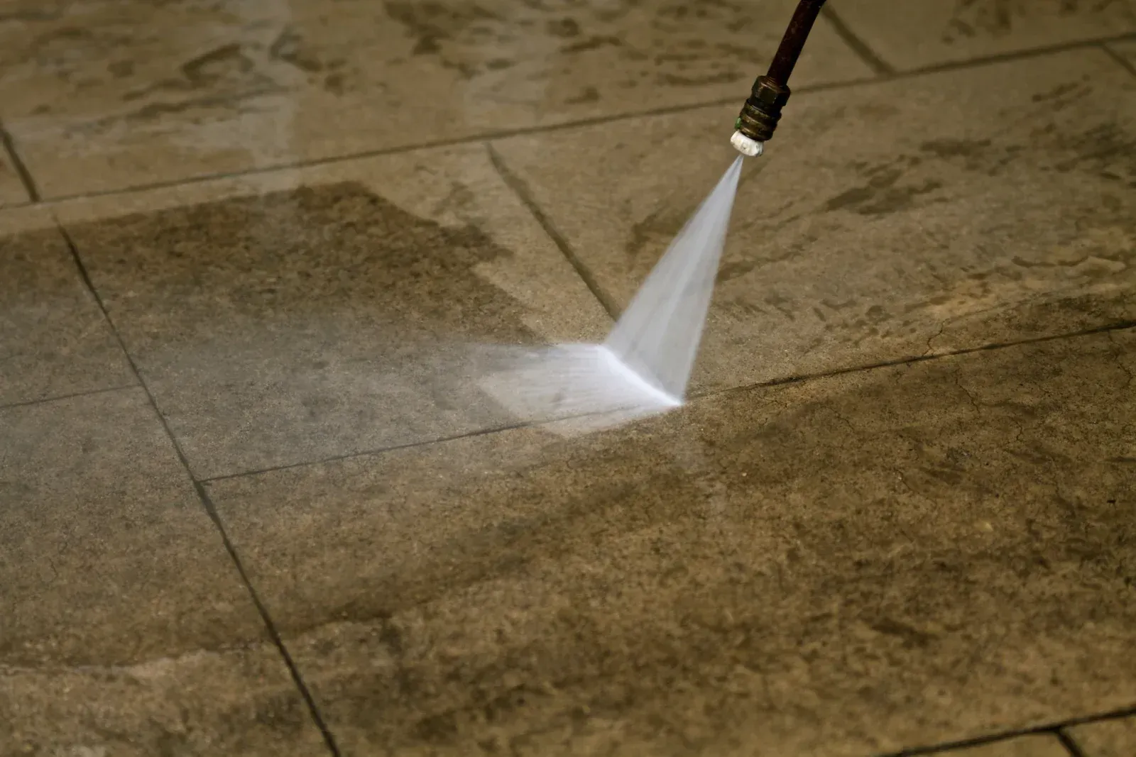 Pressure washer spraying water on stone tiles.
