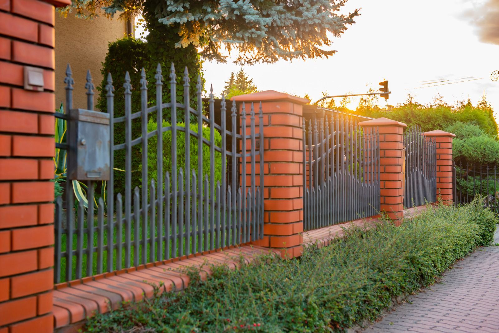 Brick and wrought iron fence with hedges. Setting sun in the background.