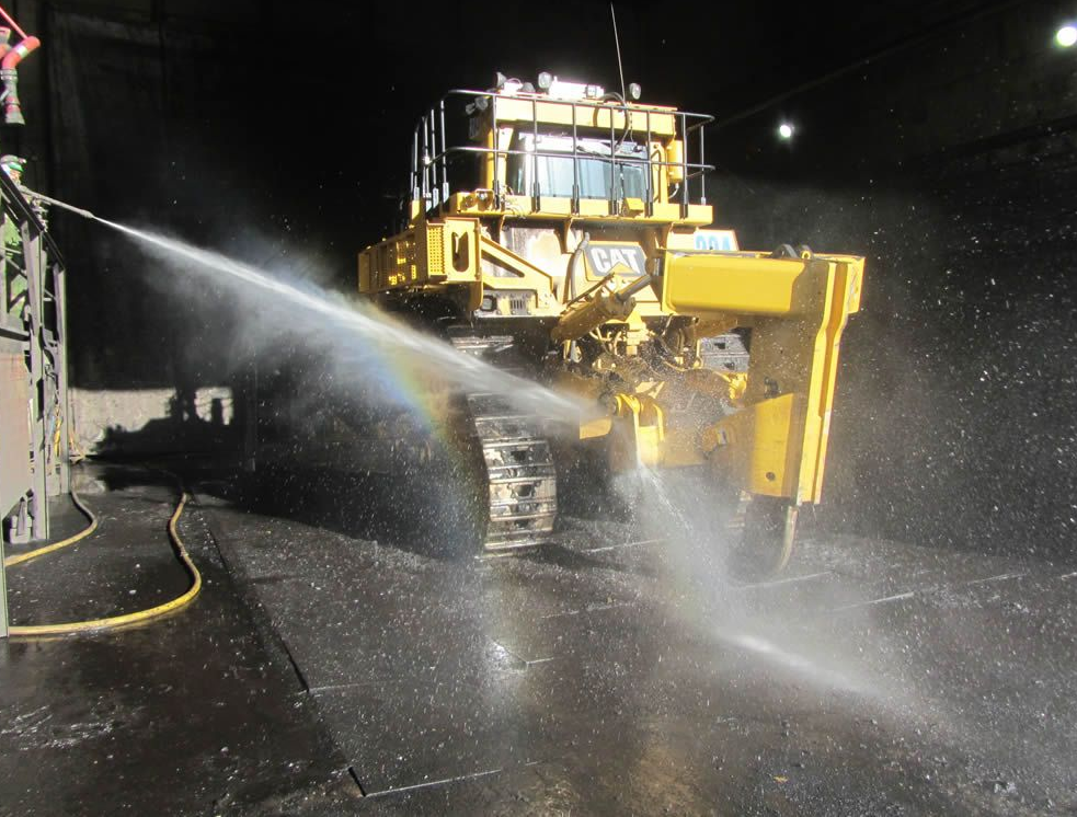 Yellow Caterpillar bulldozer being sprayed with water in a dark tunnel, creating a mist.