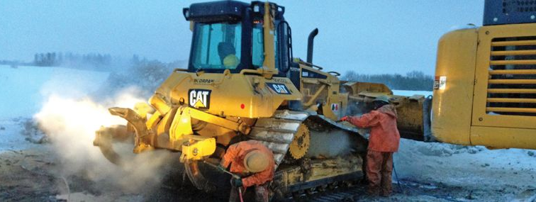 Yellow Caterpillar bulldozer with two workers in orange suits, in a snowy field.