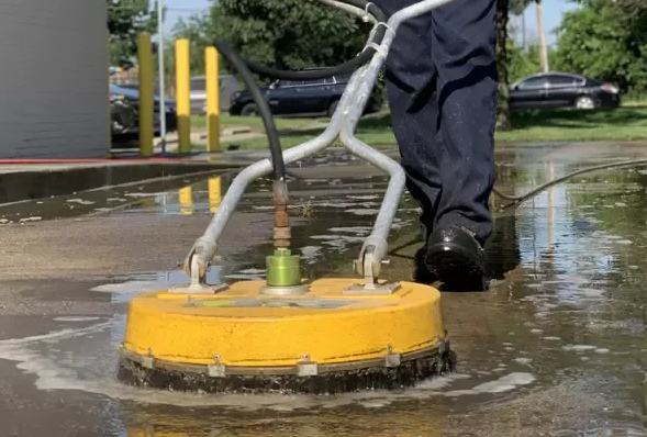 A person uses a yellow surface cleaner to wash a concrete surface outdoors.
