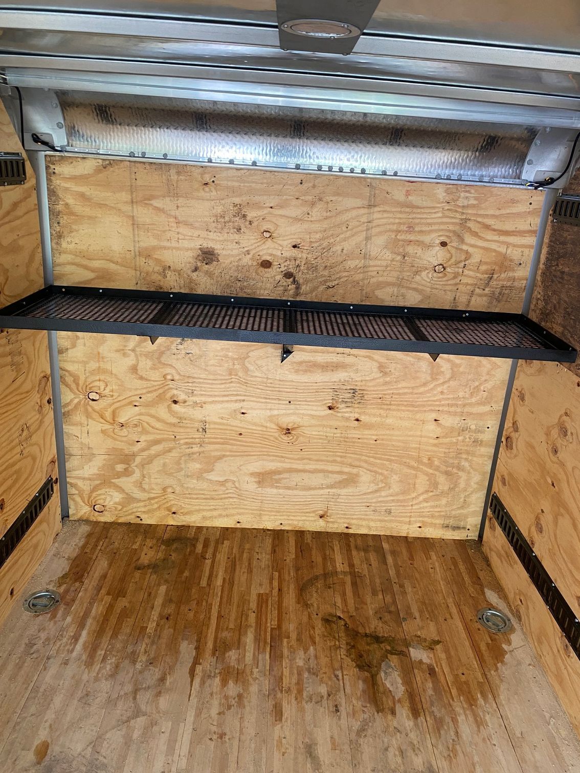 the inside of a trailer with a wooden floor and a metal shelf .