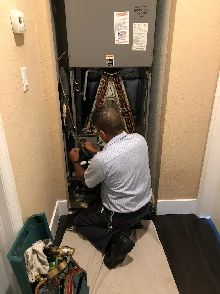 HVAC technician working on an air handler unit in a closet. Green toolbox and white rug are visible.