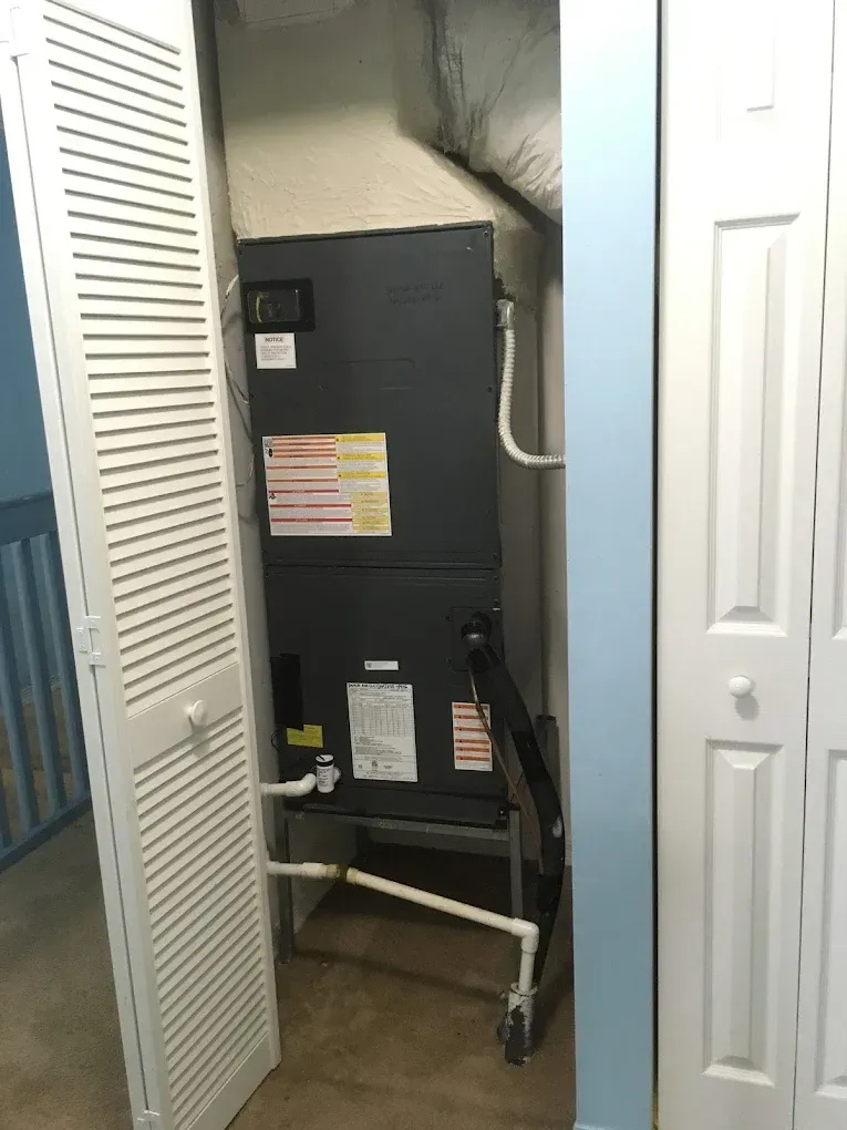 HVAC unit in a closet with white louvered doors, white pipes, and a blue wall.