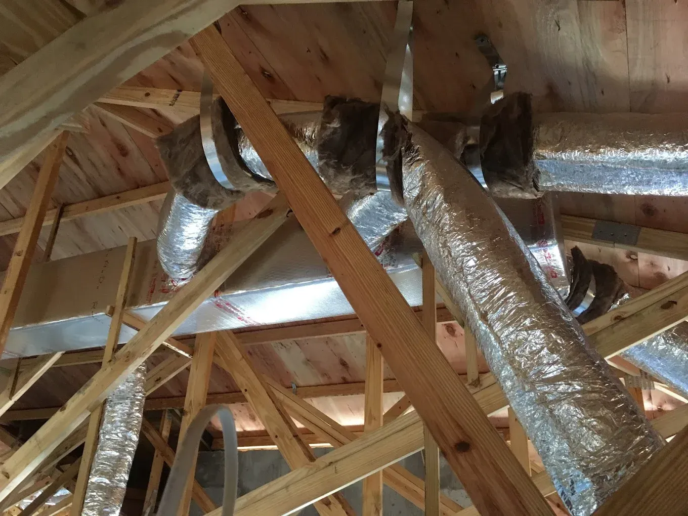 HVAC ductwork installed in an attic; flexible silver ducts attached to wooden framing.