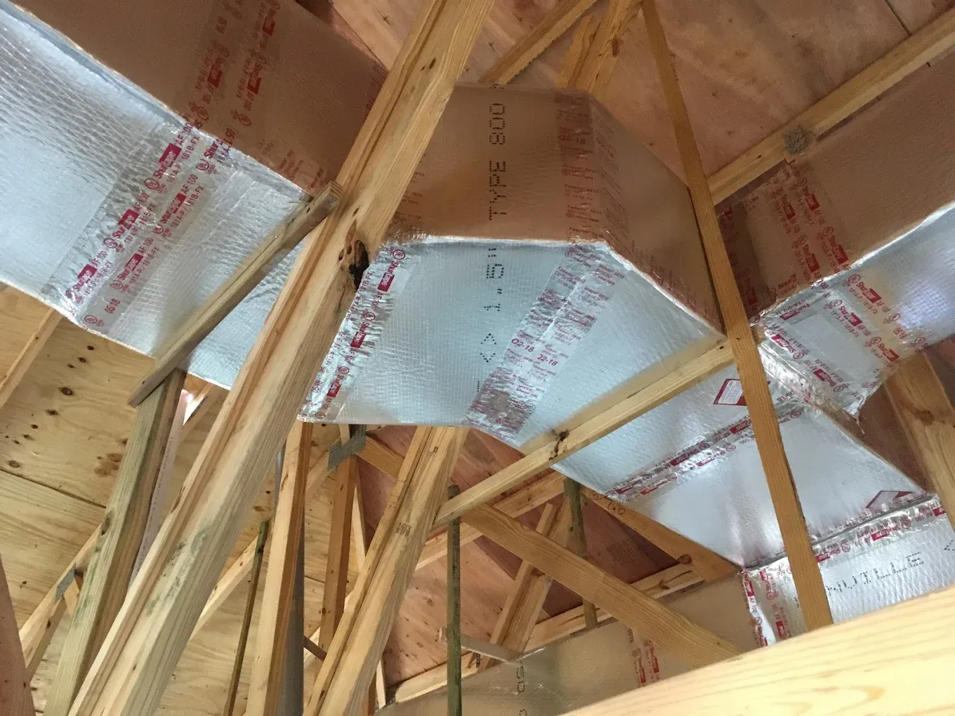 Wooden rafters in an attic with reflective insulation installed between them.