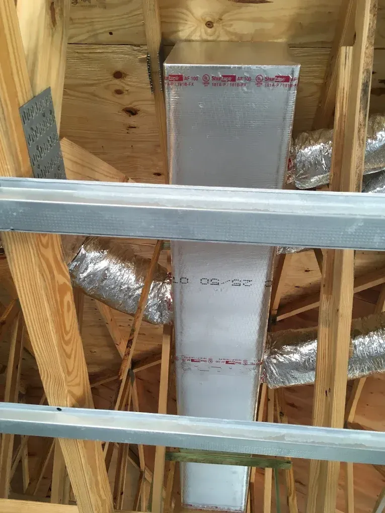 HVAC ductwork in attic, rectangular and silver, surrounded by wooden rafters and insulation.