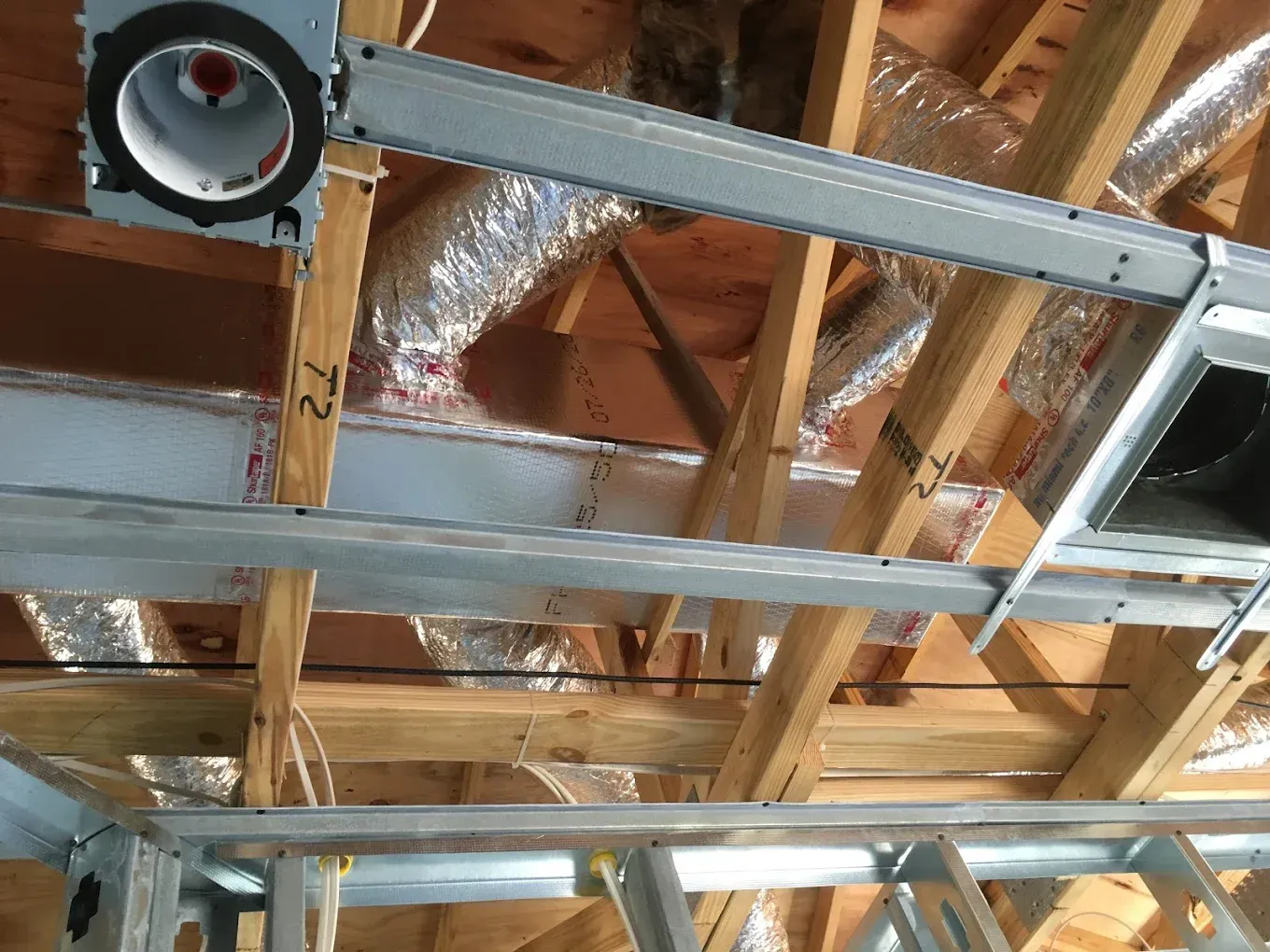 HVAC ductwork installation in an unfinished attic; metal framing and insulated ducting visible.