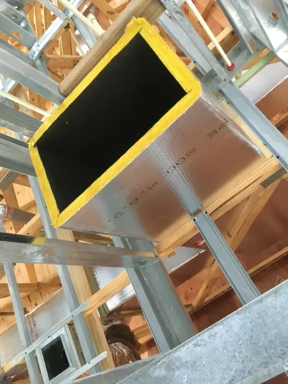 Insulated HVAC ductwork, yellow trim, installed in a new building frame of wood and metal studs.