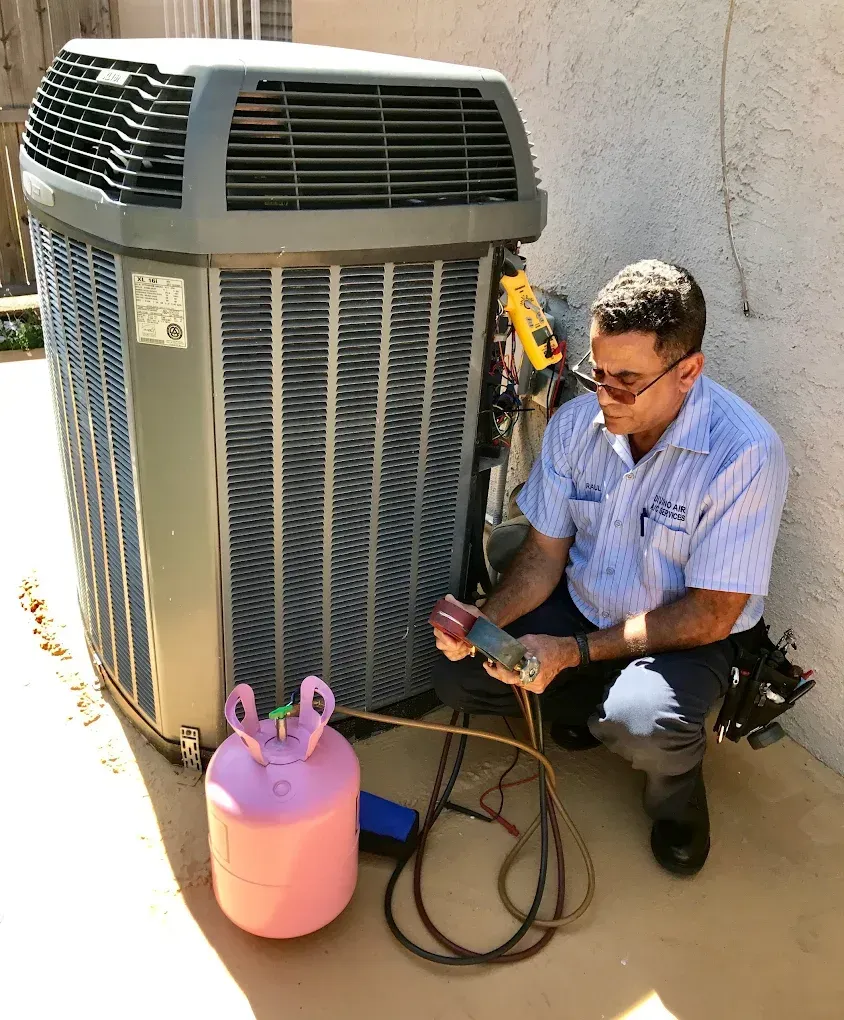 HVAC technician near an air conditioning unit; pink refrigerant tank connected to gauges.