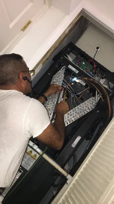 A person in a white shirt repairs an air conditioning unit. Inside room.