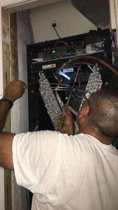 Person soldering wires inside a black electronic panel in a narrow doorway.