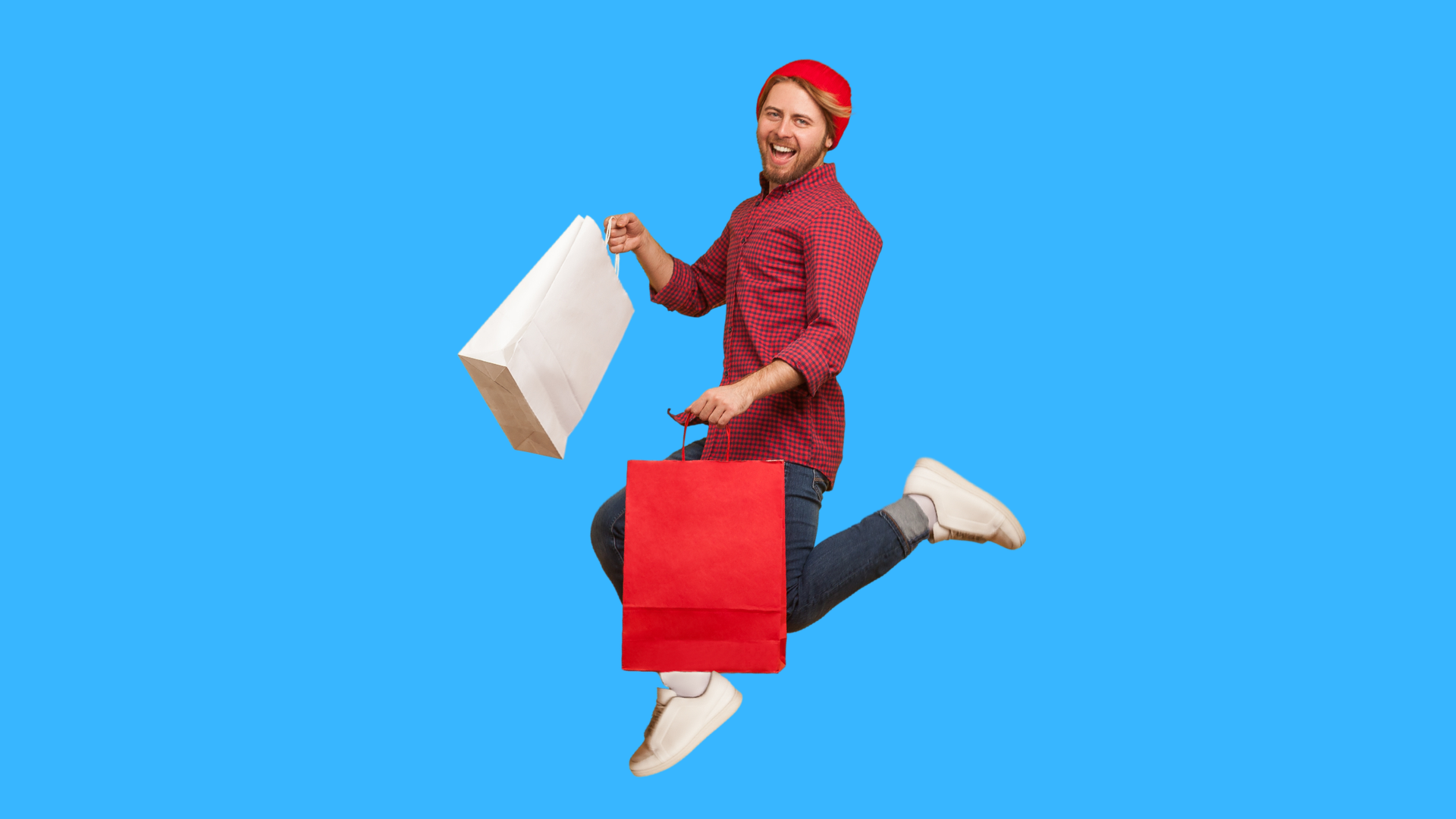A person in a red shirt and beanie leaps against a blue background, holding white and red shopping bags.