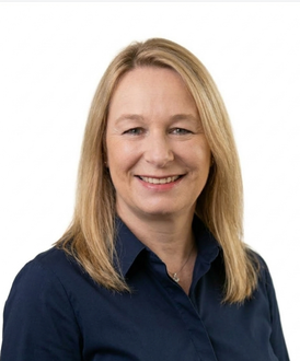 A smiling person with shoulder-length blonde hair, wearing a navy blue blazer over a maroon top, against a white background.