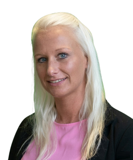 A person with long blonde hair, wearing a pink top and black blazer, smiling slightly against a plain white background.