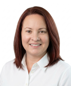 Professional headshot of a person with auburn hair, wearing a navy blue blazer and white top against a white background.