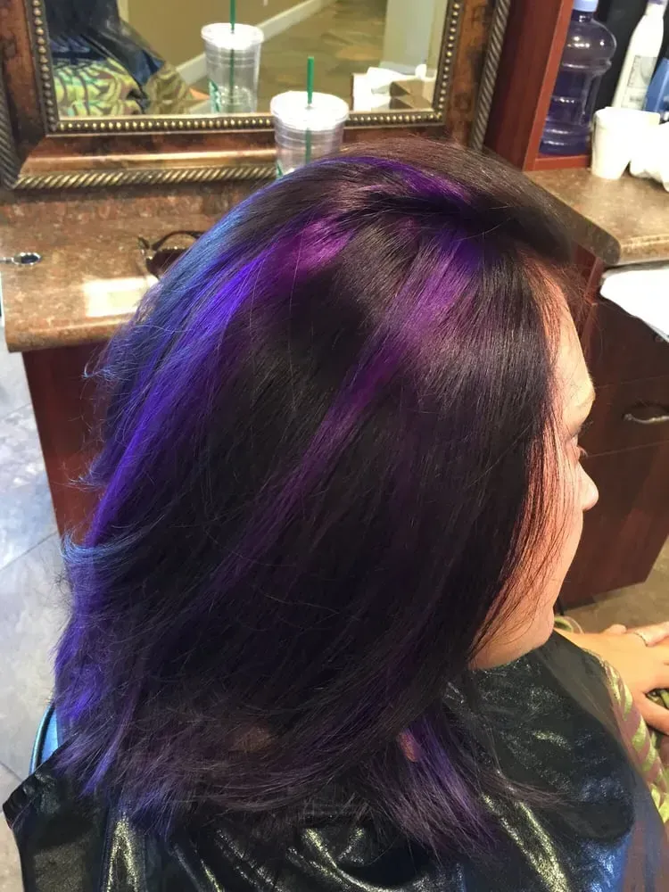 A woman with purple hair is sitting in front of a mirror.