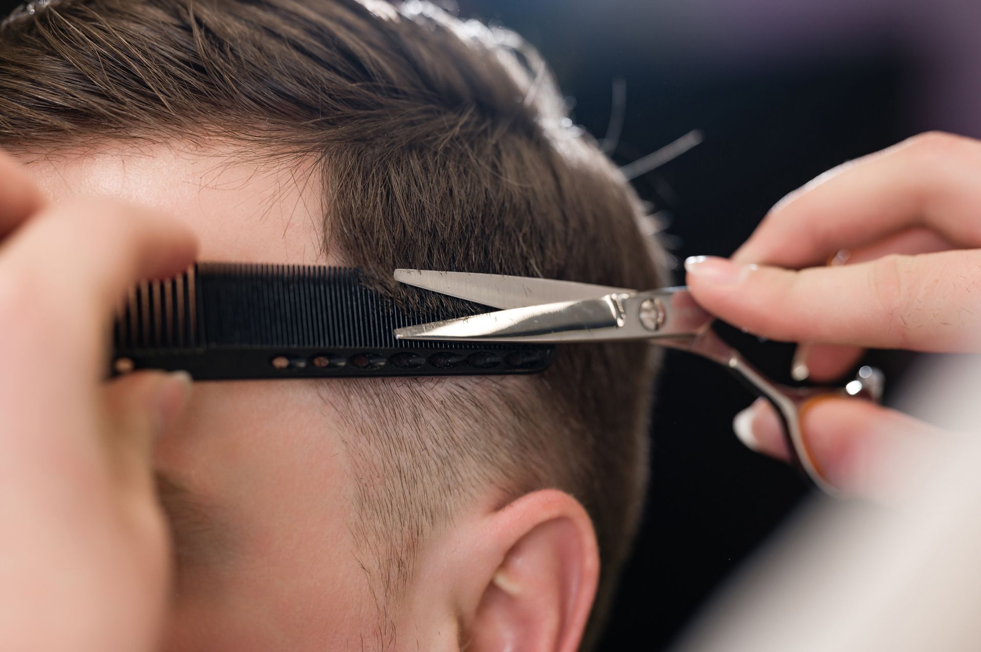 A man is getting his hair cut by a barber with scissors and a comb.