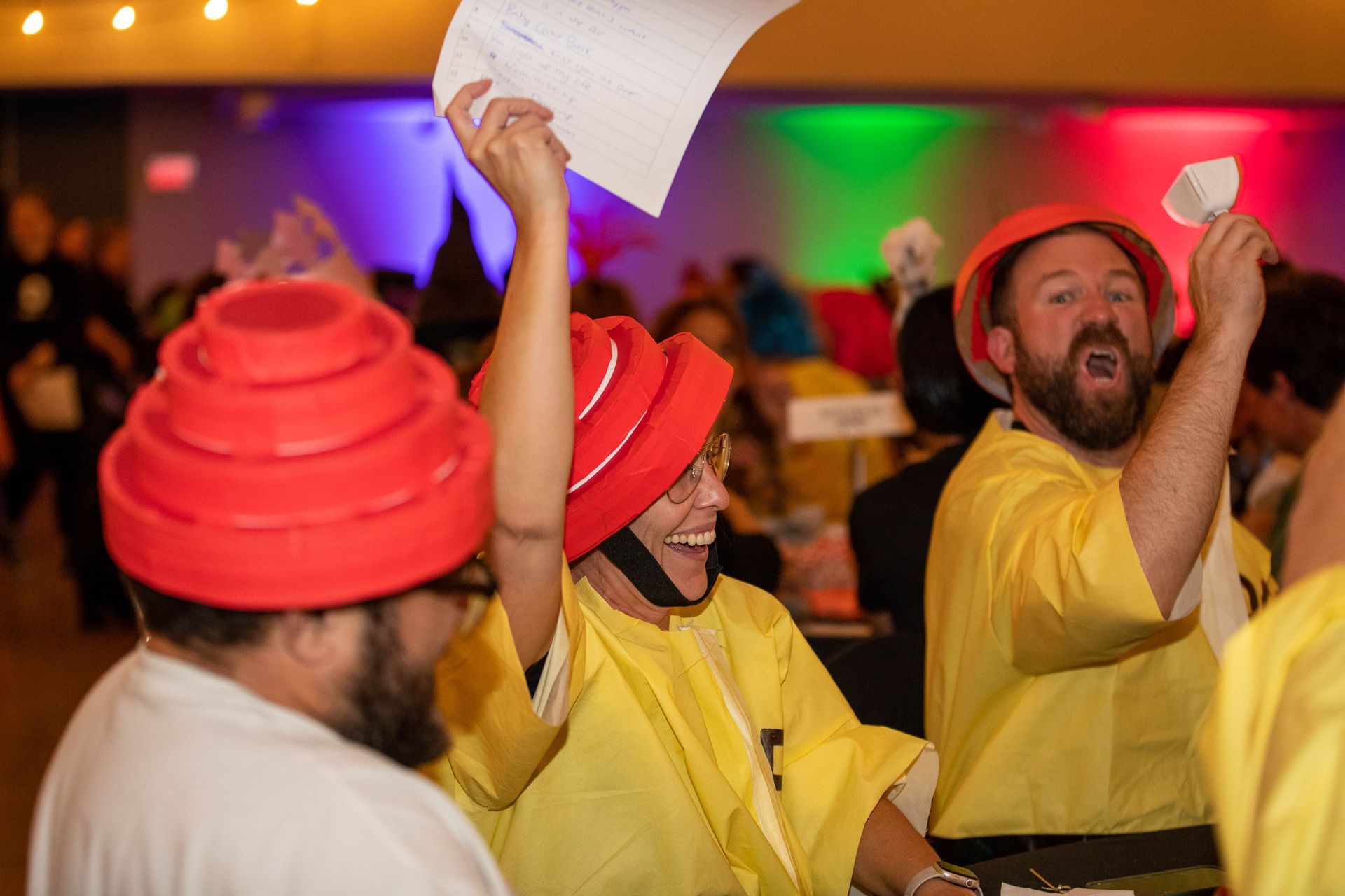 A group of people wearing red hats and yellow shirts are dancing in a room.