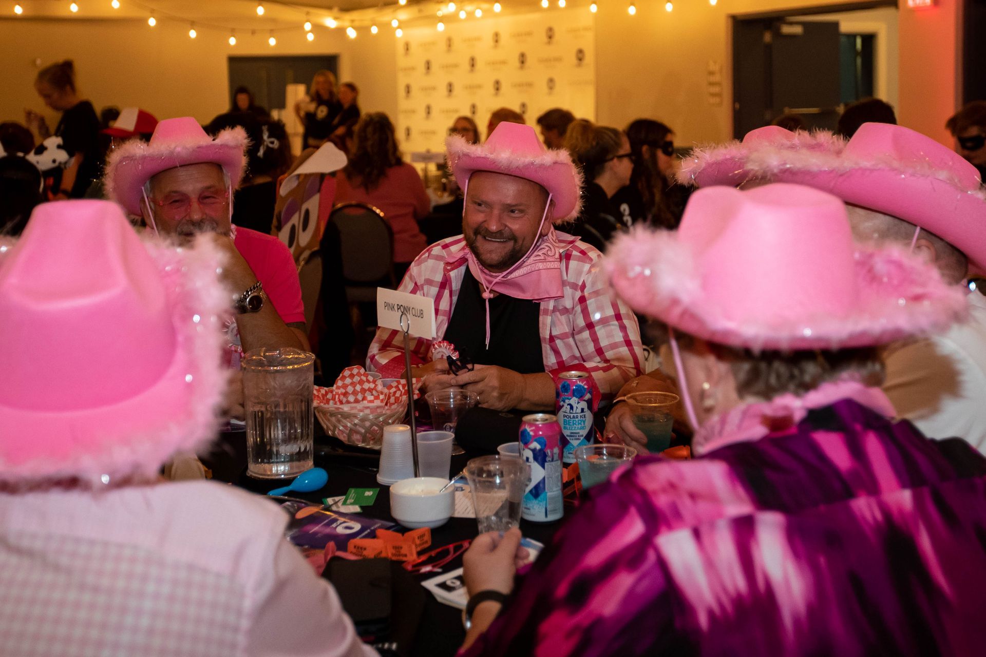 A group of people wearing pink cowboy hats are sitting at a table.