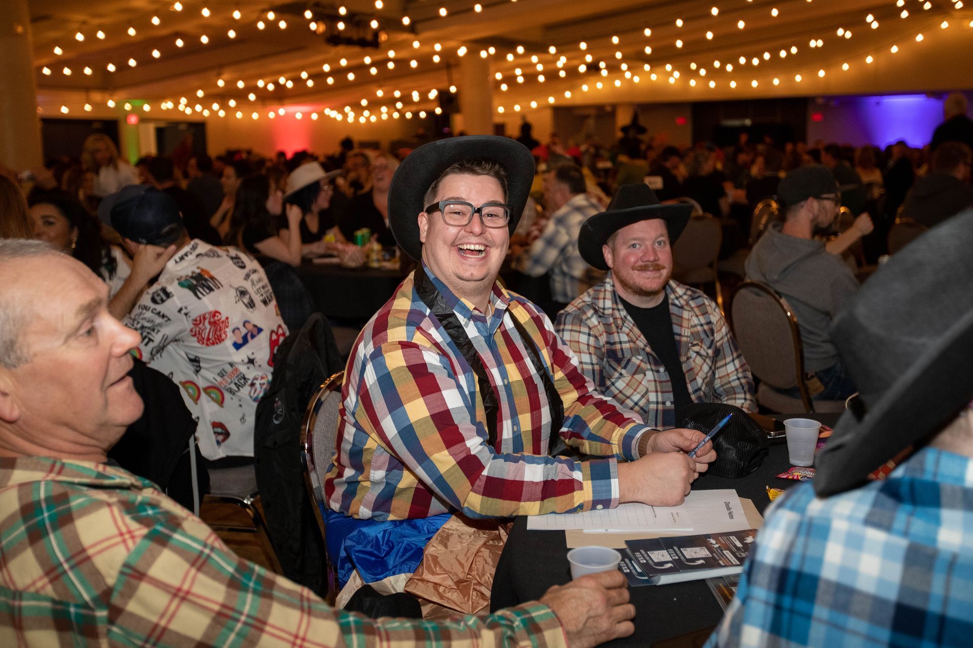 A group of people dressed as cowboys are sitting at tables in a room.