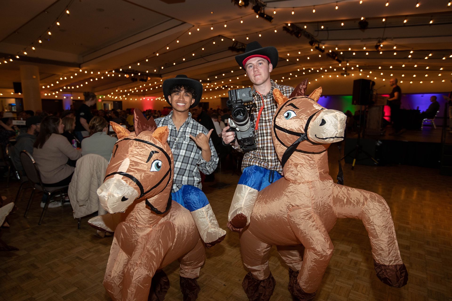 Two people dressed as cowboys are riding inflatable horses.