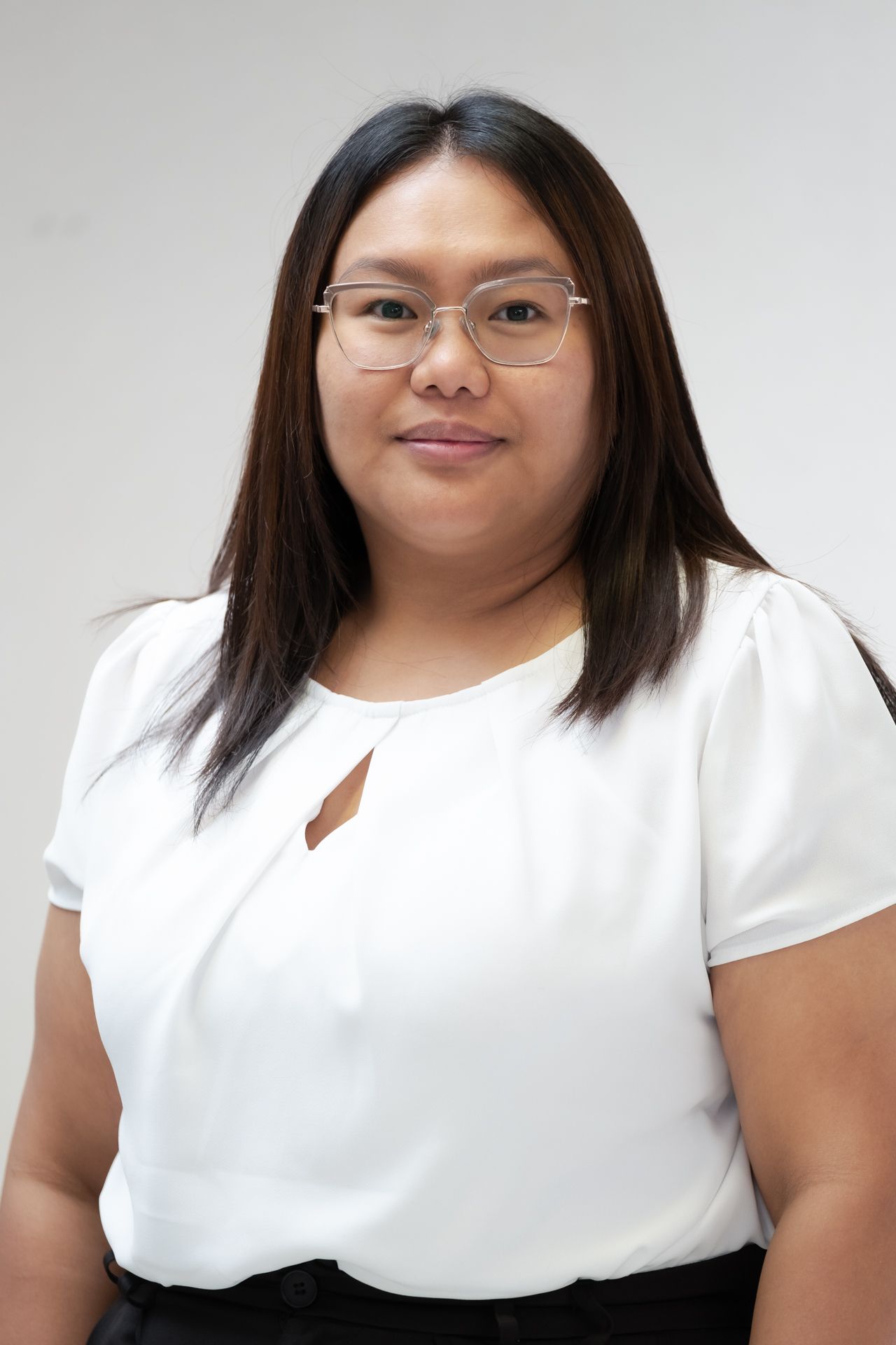 A woman wearing glasses and a white shirt is smiling for the camera.
