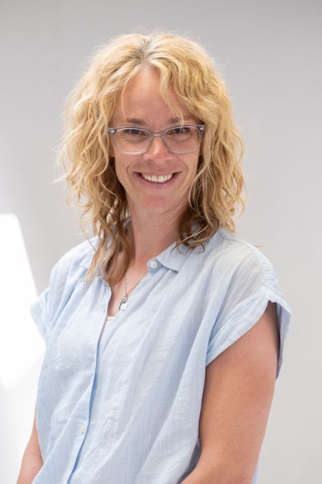 A woman wearing glasses and a blue shirt is smiling for the camera.