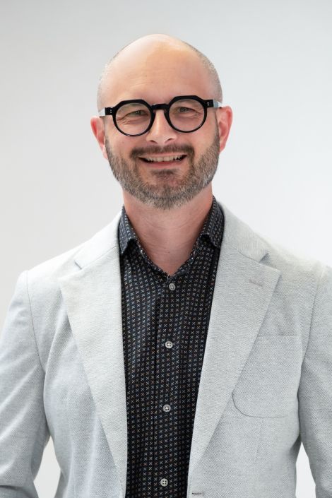 A bald man with glasses and a beard is smiling for the camera.