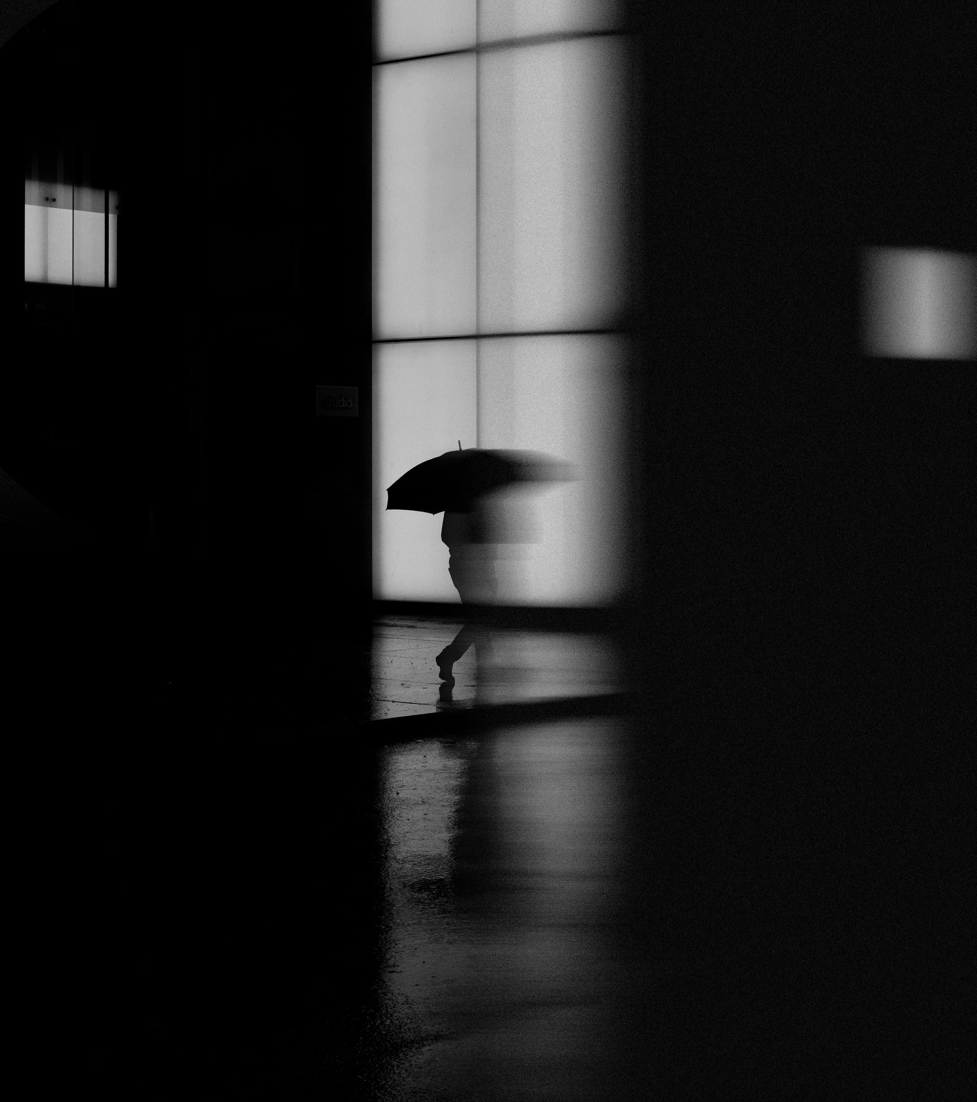 A black and white photo of a person walking in the rain with an umbrella.